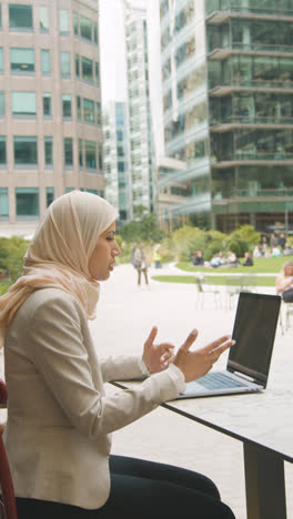 Vertical-Video-Of-Muslim-Businesswoman-Sitting-Outdoors-In-City-Gardens-Making-Video-Of-Call-On-Laptop